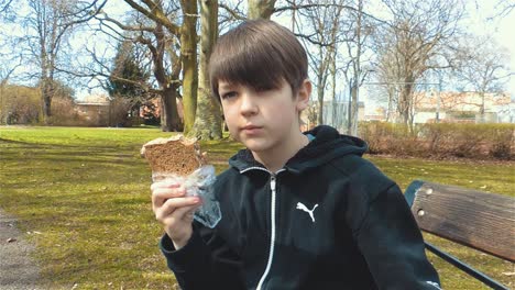 caucasian young boy eating sandwich outdoors and drinking energy drink