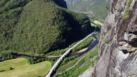 antena en movimiento descendente a lo largo de la pared de la montaña - observando la autopista noruega e-16 entre bergen y voss con el ferrocarril y el río salmon a los lados - paisaje espectacular