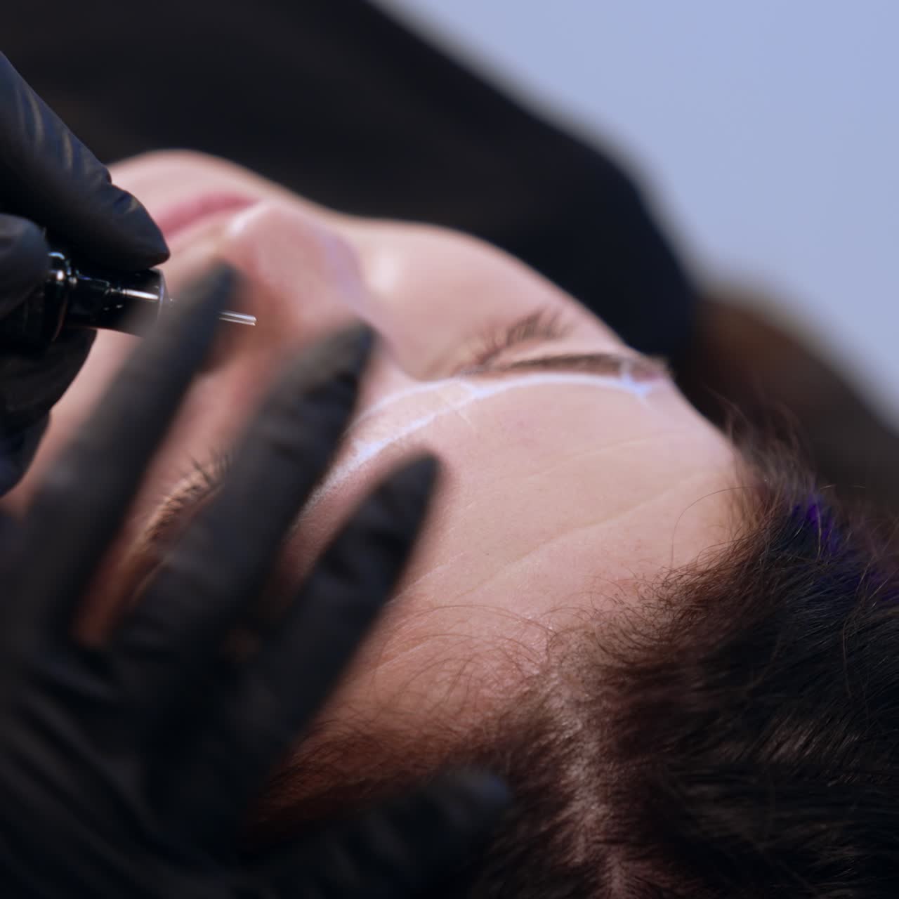 Beautician uses a special device to apply permanent make up on client's eyebrows. Salon beauty procedure. Close up