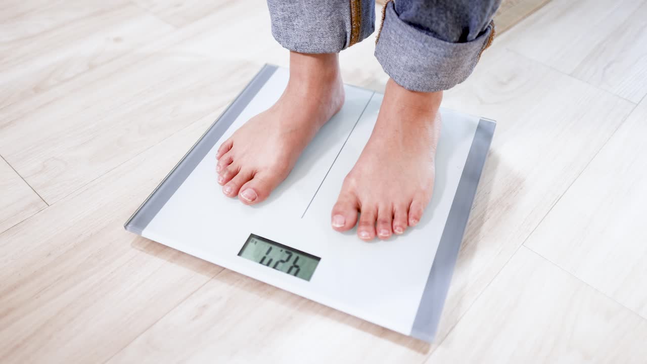 Close-up shot of bare feet stepping onto a digital scale on a wooden floor