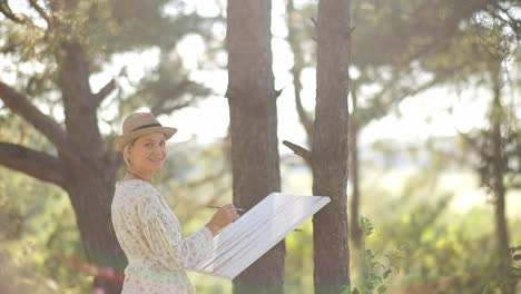 cheerful female artist paints an oil painting on canvas in the forest the girl holds a brush in her - cheerful female artist paints an oil painting on canvas in the forest. the girl holds a brush in her hands. creative mood