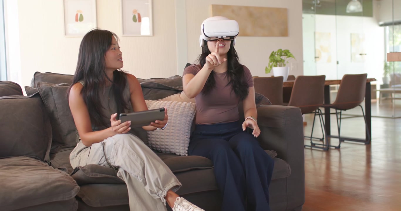 Asian women sitting on couch at home, tablet starting VR to explore world, white headset gesturing
