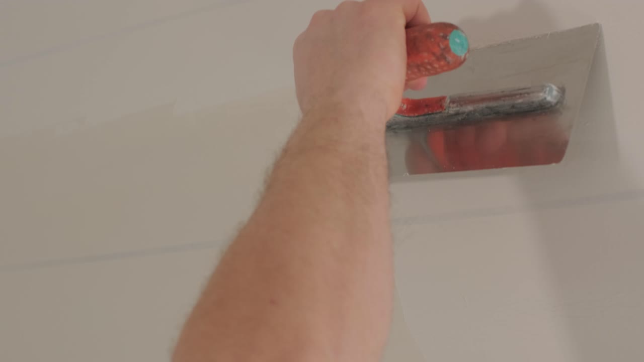 hombre enyesando las paredes con la masilla de acabado en la habitación con la espátula de masilla