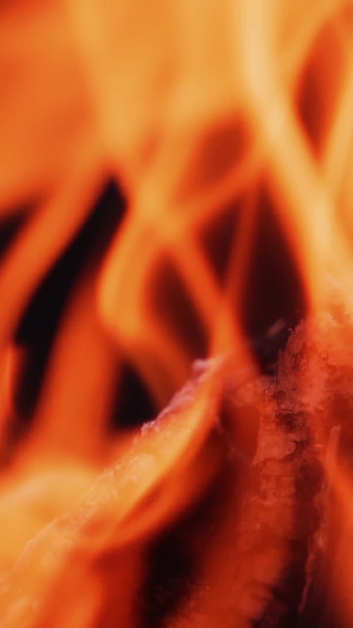 Close-up blur bright flame. Vivid flame of bonfire on dark background. Detailed motion of yellow and red fire. Slow motion. Vertical video