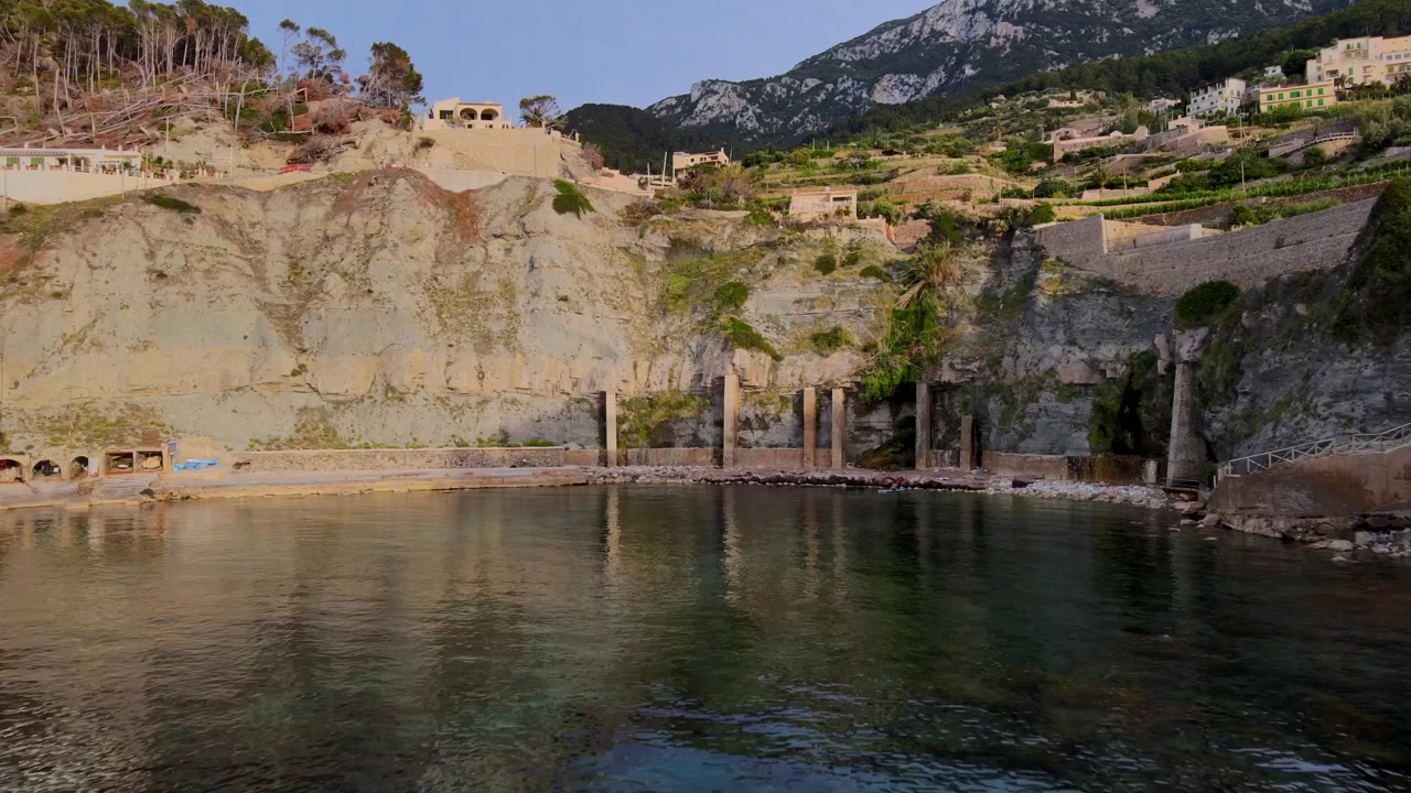 Staňte se svědky úchvatných výhledů na Banyalbufar, Mallorca, jak slunce zapadá nad klidným pobřežím. Klidné vody odrážejí zářivé barvy oblohy a osvětlují svěží krajinu.