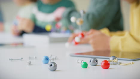 primer plano de estudiantes de primaria estudiando modelos moleculares en la clase de ciencias con una tableta digital