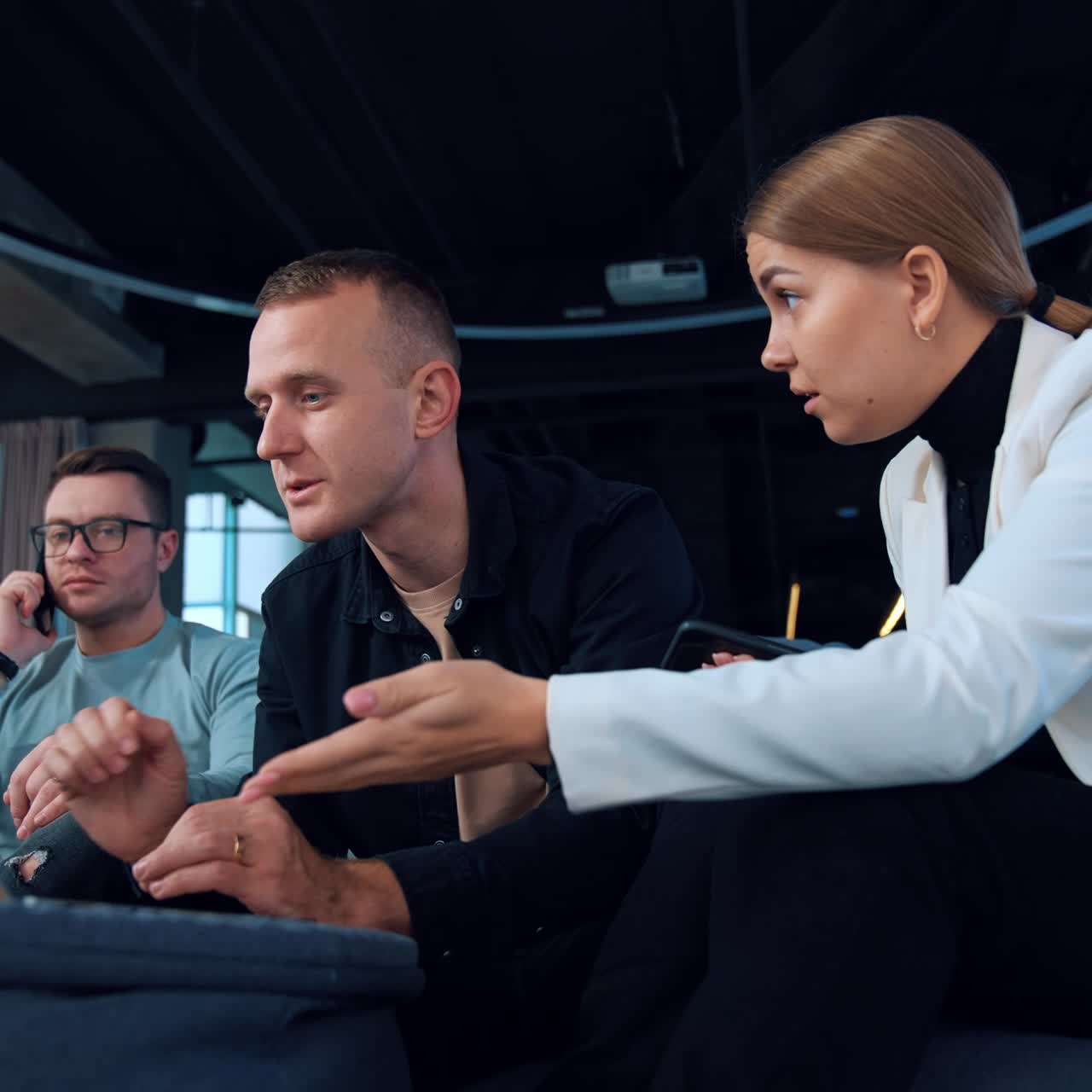 Business team sitting together in office discussing work issues. People look at the laptop talking and laughing. Man behind speaks on the phone. Low angle view