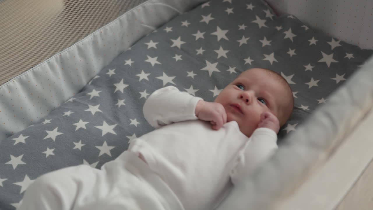 Primo piano di un neonato sdraiato in una culla con una coperta a fantasia stellata che guarda in alto con curiosità