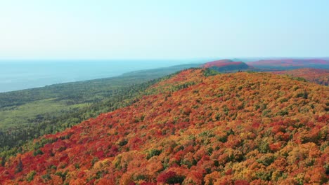 Vasto-Bosque-Con-Colores-Cambiantes-De-Otoño,-Paisaje-Con-Colinas-Onduladas-Y-Costa-De-Lago-En-El-Horizonte---Toma-Aérea-De-Drones