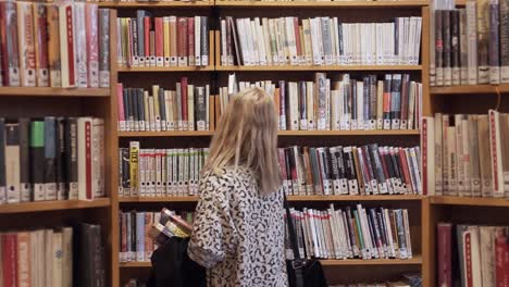 una joven caminando entre estanterías en la biblioteca, con una plataforma rodante con libros por todas partes