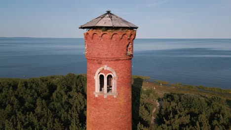 sinkender flug entlang eines leuchtturms an der küste von estland - alter verlorener leuchtturm mit rotem stein und ohne fenster, im sommer von drohne aufgenommen