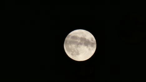 Full-harvest-moon-crater-surface-closeup-passing-across-dark-sky-cloud-in-foreground