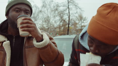 Young-African-American-Men-Having-Snack-and-Chatting-by-Car