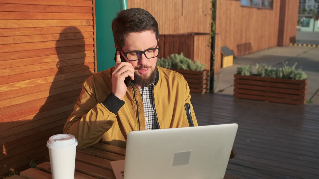 hombre trabajando al aire libre en una computadora portátil mientras hace una llamada telefónica