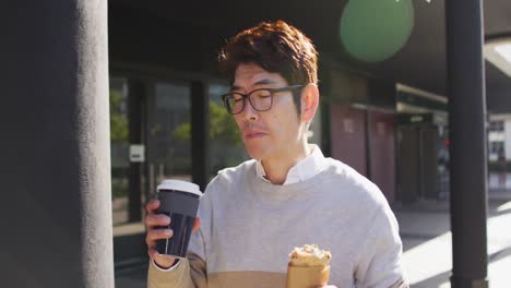 asian man drinking coffee and having a snack while walking outdoors