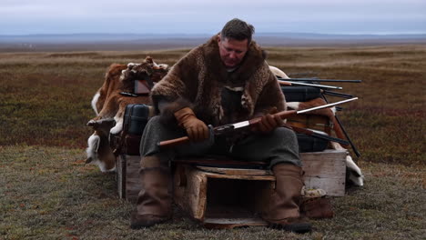 a hunter in a fur coat preparing his rifle in a remote wilderness setting