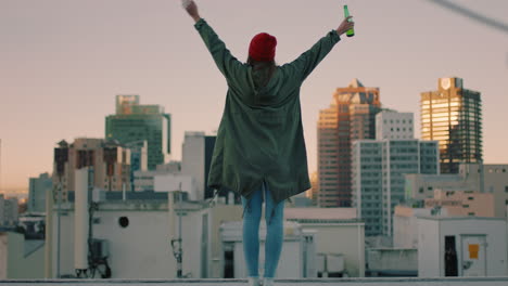 Mujer-Joven-Feliz-Caminando-En-La-Azotea-Con-Los-Brazos-Levantados-Celebrando-La-Libertad-Disfrutando-De-Pasar-El-Rato-Bebiendo-Alcohol-Mirando-El-Horizonte-Urbano-De-La-Ciudad-Al-Atardecer