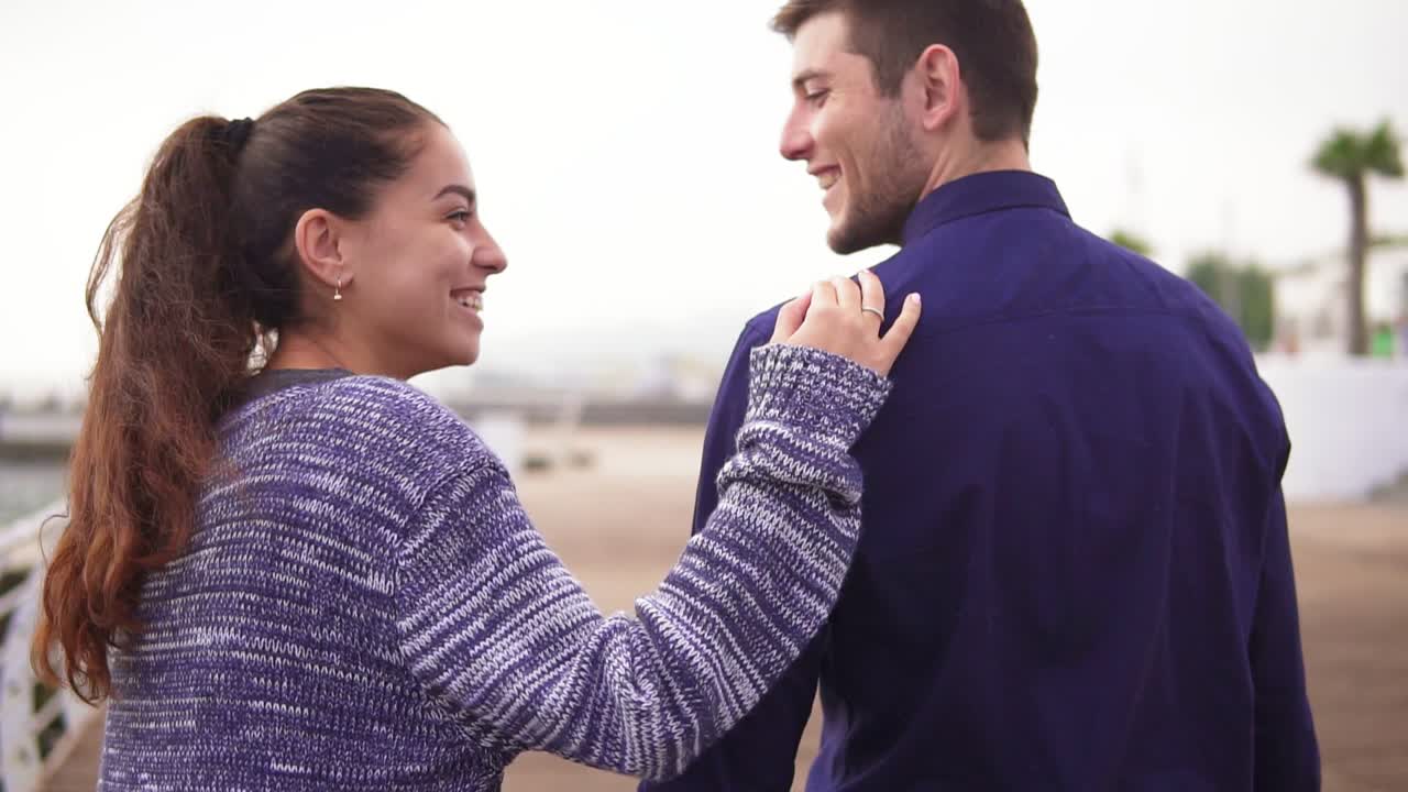 vista de fondo de una joven y hermosa pareja caminando juntos, abrazándose y hablando mirándose a los ojos y sonriendo
