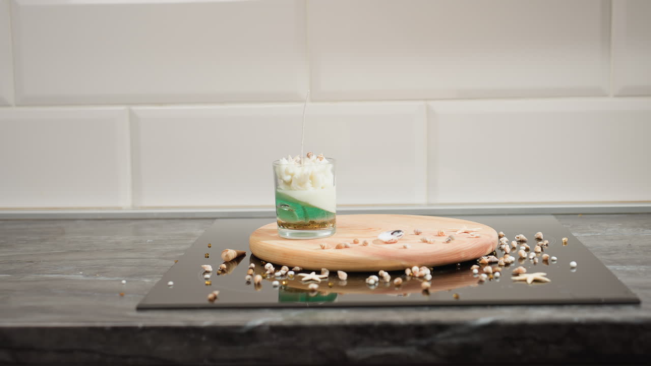 Decorator carefully places decorated cake on stainless tray surrounded by scattered edible sprinkles toppings while organizing elegant dessert presentation in clean minimalist kitchen