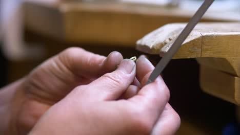 male jewelry maker hand filing a piece of jewellery in a workshop