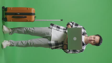 full body of asian male traveler with luggage using a laptop then smiling to camera while standing in the green screen background studio