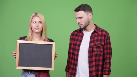 young couple holding blackboard and looking shocked together