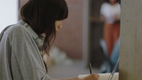 Una-Joven-Mujer-De-Negocios-Escribiendo-Notas-Disfrutando-Del-Estudio-Usando-Una-Computadora-Portátil-Trabajando-En-Un-Proyecto-De-Intercambio-De-Ideas-En-Una-Oficina-Ocupada