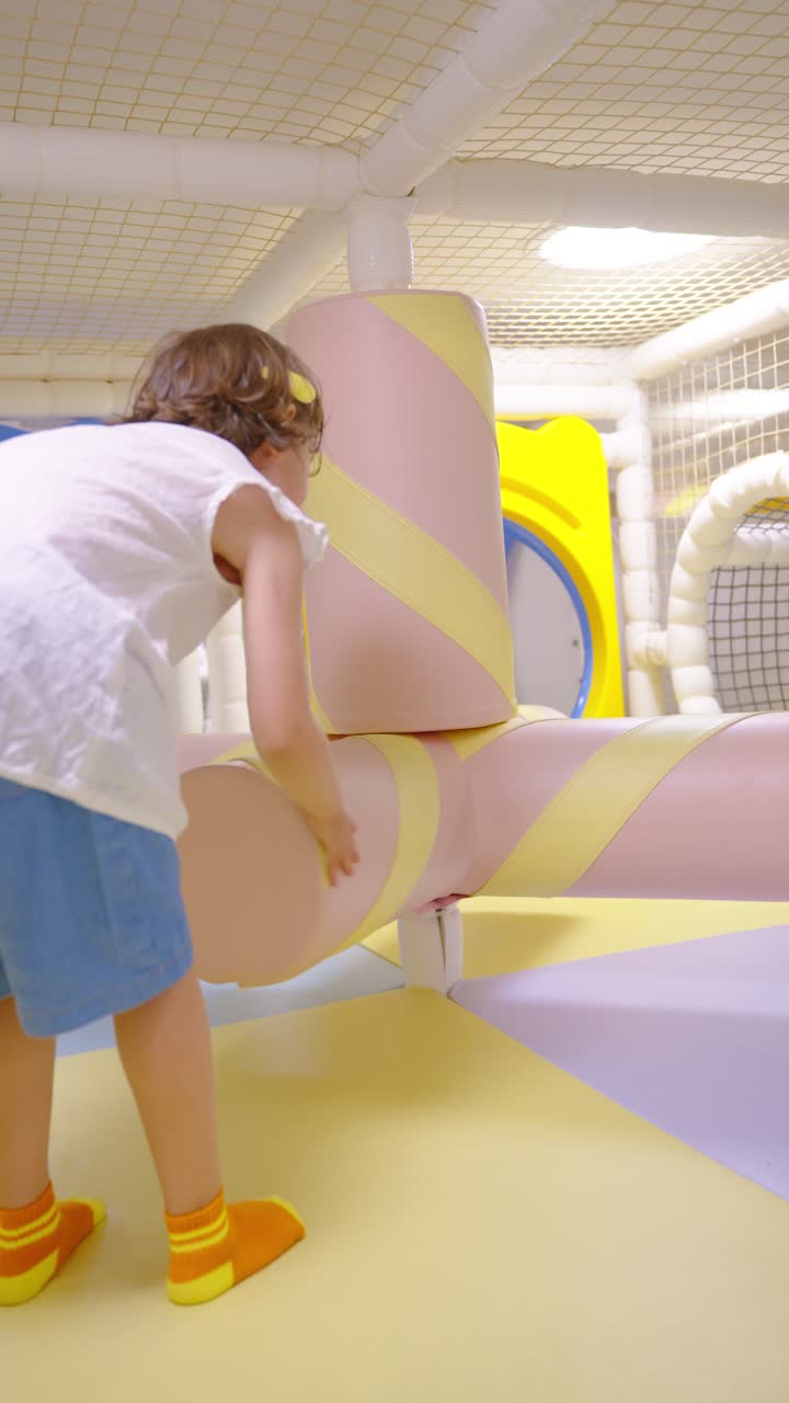 5-year-old girl spins soft marshmallow-shaped element in colorful indoor playground with safe padded play equipment