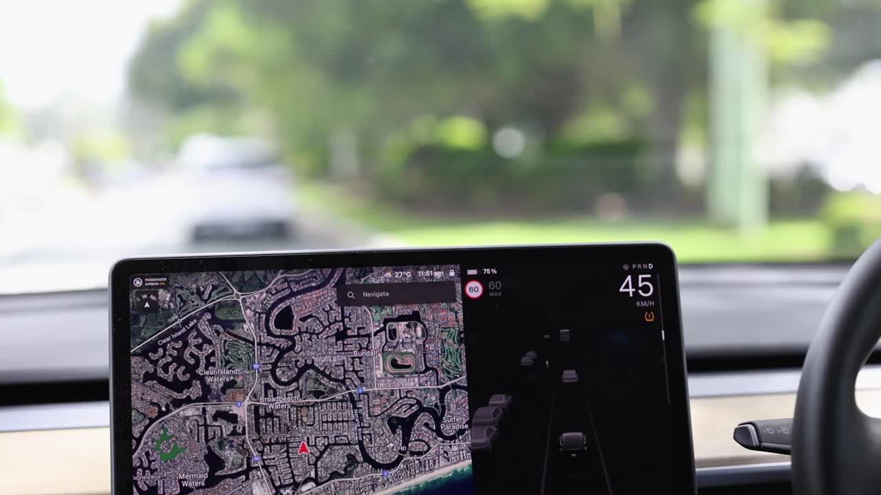 A car navigates Gold Coast streets using a digital map display. Bright daylight illuminates the lush surroundings