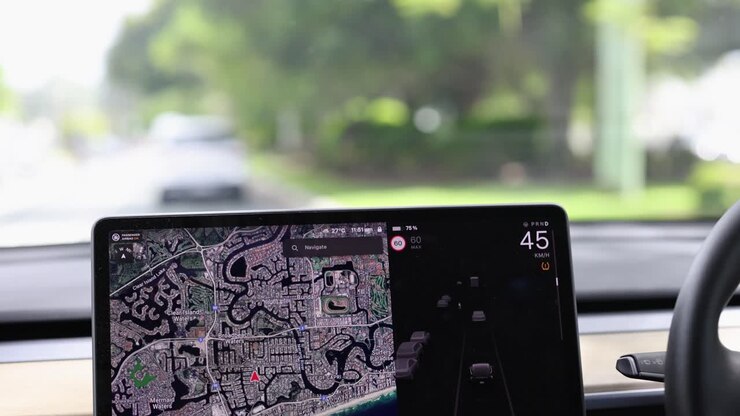 A car navigates Gold Coast streets using a digital map display. Bright daylight illuminates the lush surroundings
