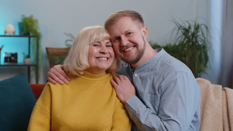 Portrait-of-senior-grandmother-with-young-adult-man-grandson-smiling-happy-embracing-hugging-at-home