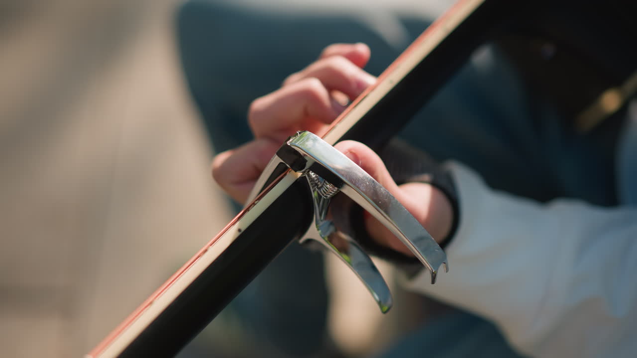 closeup acoustic guitar neck capo placed on fretboard, hand adjusting capo during outdoor practice session, warm sunlight on wooden grain, shallow depth of field, lofi intimate atmosphere