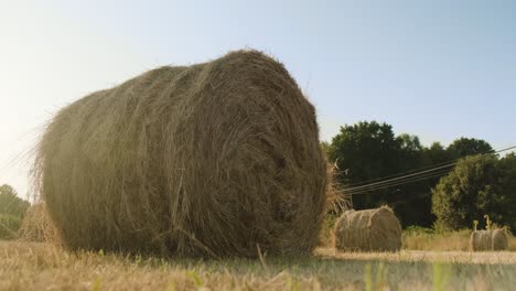 Sunbeam-through-Roll-stacks-of-wheat-straws-on-countryside-field,-Low-angle-view