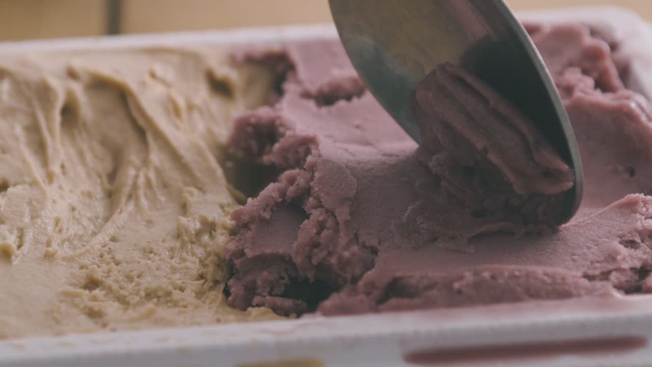 Un cucchiaio preleva una porzione di gelato artigianale italiano nei gusti nocciola, pistacchio e fragola da una vaschetta.