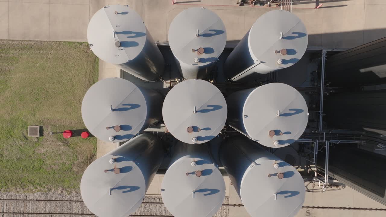 Abstract top-down aerial shot of cylindrical industrial storage tanks and their long shadows, highlighting chemical storage and geometric symmetry at a facility