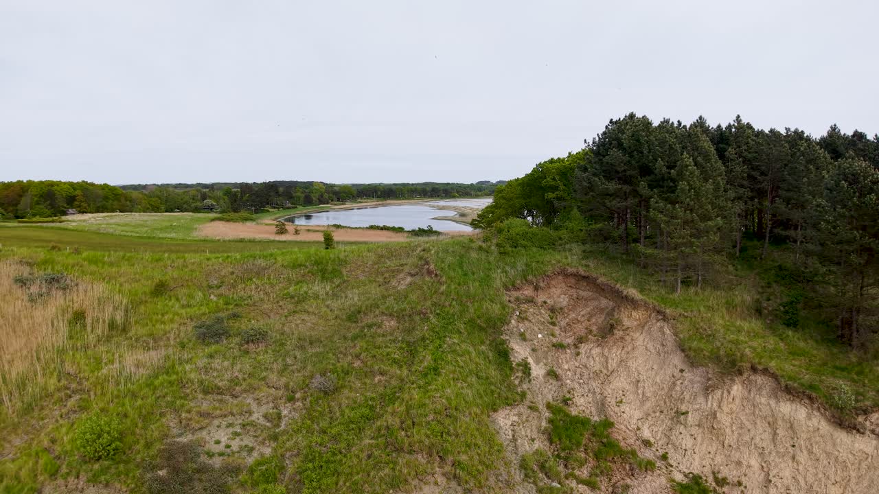 Drone footage overlooking rugged cliffs, pine trees, and a calm inlet within Denmark’s Mols Bjerge National Park