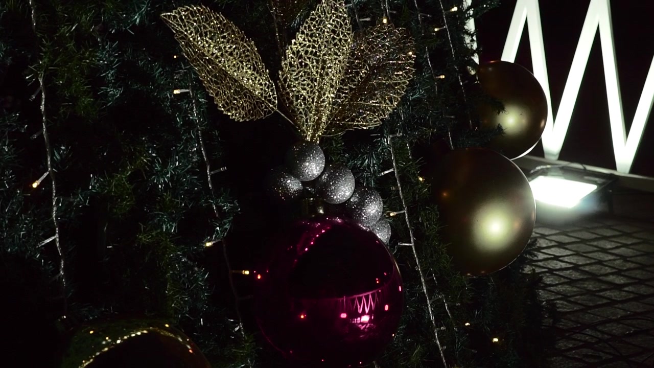 Primo piano di ornamenti per albero di Natale con palline rosse e dorate, foglie glitterate e luci calde, creando un'elegante scena di decorazione natalizia.