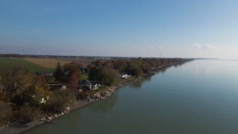 Pullbak-Aéreo-Sobre-Casas-Costeras-Junto-Al-Lago-Con-Campos-De-Cultivo-Con-Vistas-A-Aguas-Plácidas