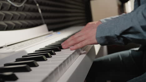 close-up of a hand wearing a blue long sleeve shirt playing a white piano, with the background showing a black acoustic wall and a hint of denim jeans.focus on the piano keys and the musician's hand