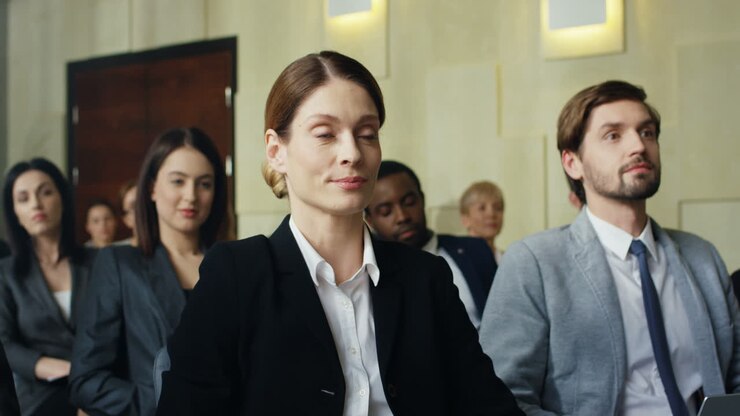 Caucasian businesswoman sitting on a chair among people in a conference room and rising his hand to ask a question