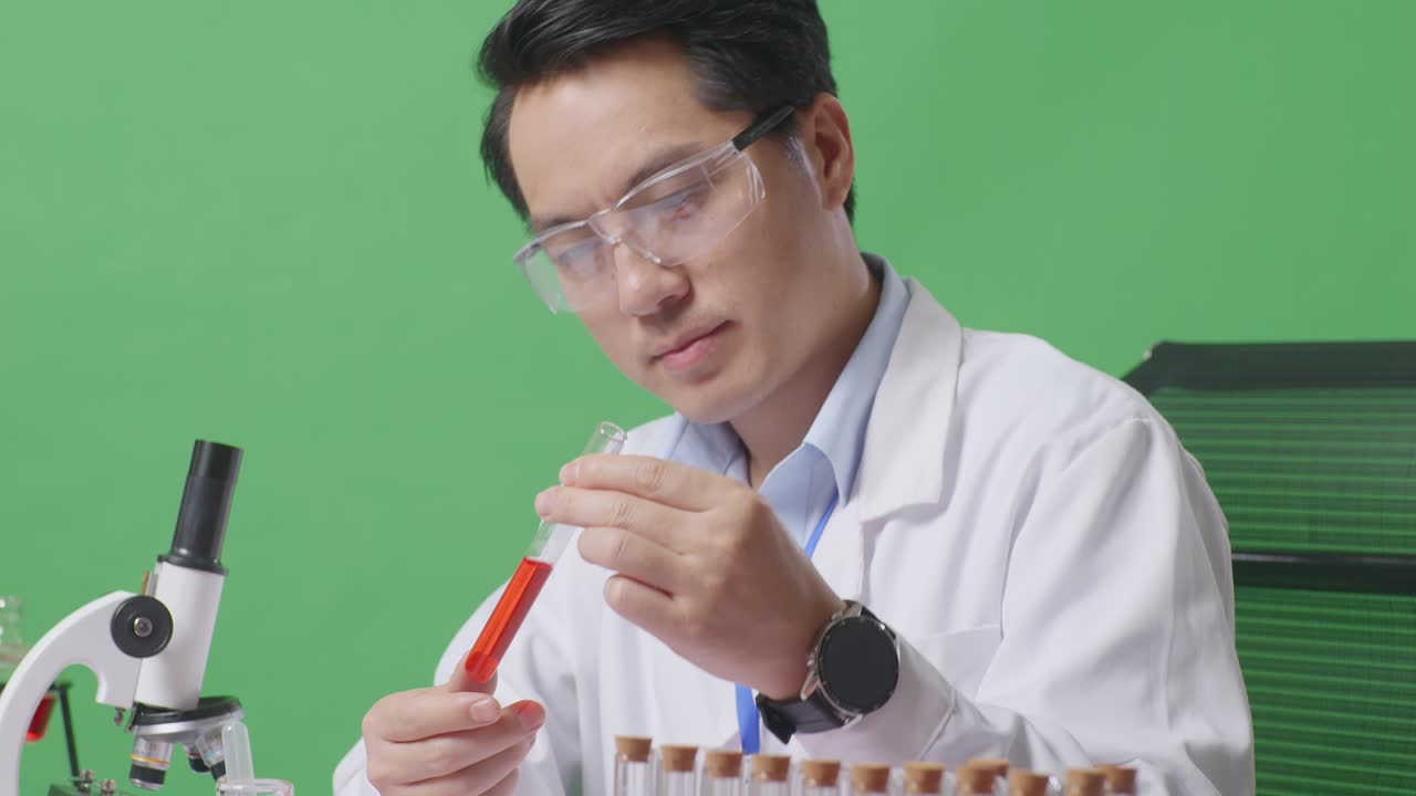 Close Up Of Side View Of Asian Man Scientist Looking At The Red Liquid In The Test Tube And Shaking Head On The Table With Microscope In The Green Screen Background Laboratory