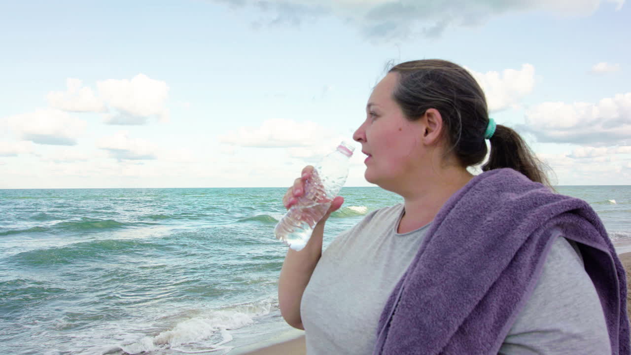 Chubby girl drinking water on the beach.