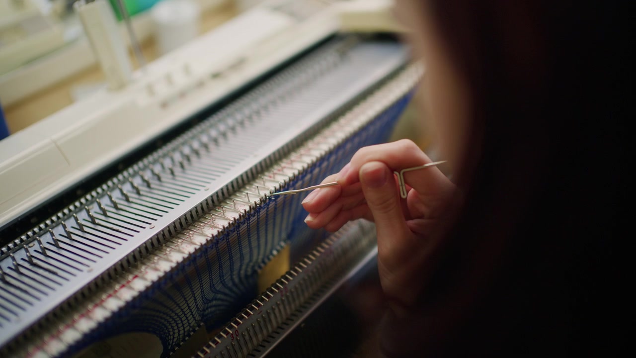 Close up of a woman adjusting blue knitted fabric on a flatbed knitting machine