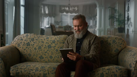 Calm senior man using tablet computer on sofa