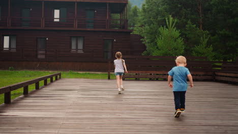 little boy chases sister running along wooden dance deck