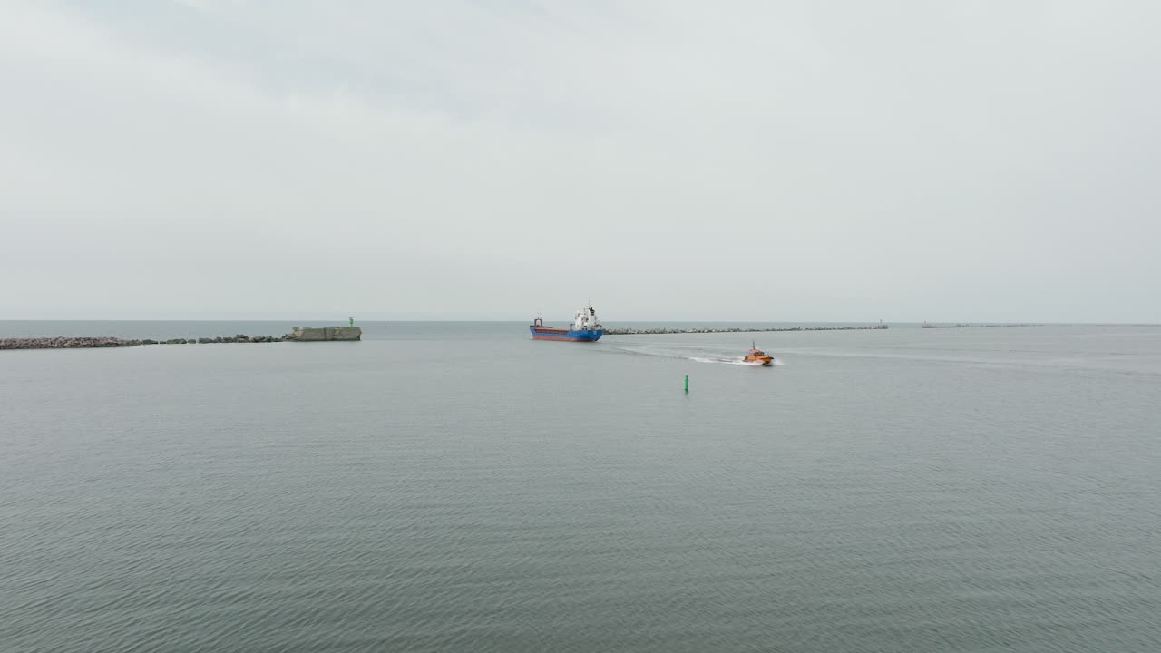 리파자 항구를 떠나는 큰 파란색 화물 선박의 공중 촬영, 카로스타 다리, 약간 구름이 쌓인 날, 평온한 발트해, 멀리 넓은 드론  ⁇  빠르게 앞으로 이동