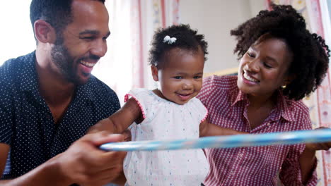 Parents-With-Baby-Daughter-Sitting-On-Floor-And-Playing-With-Hoop-At-Home