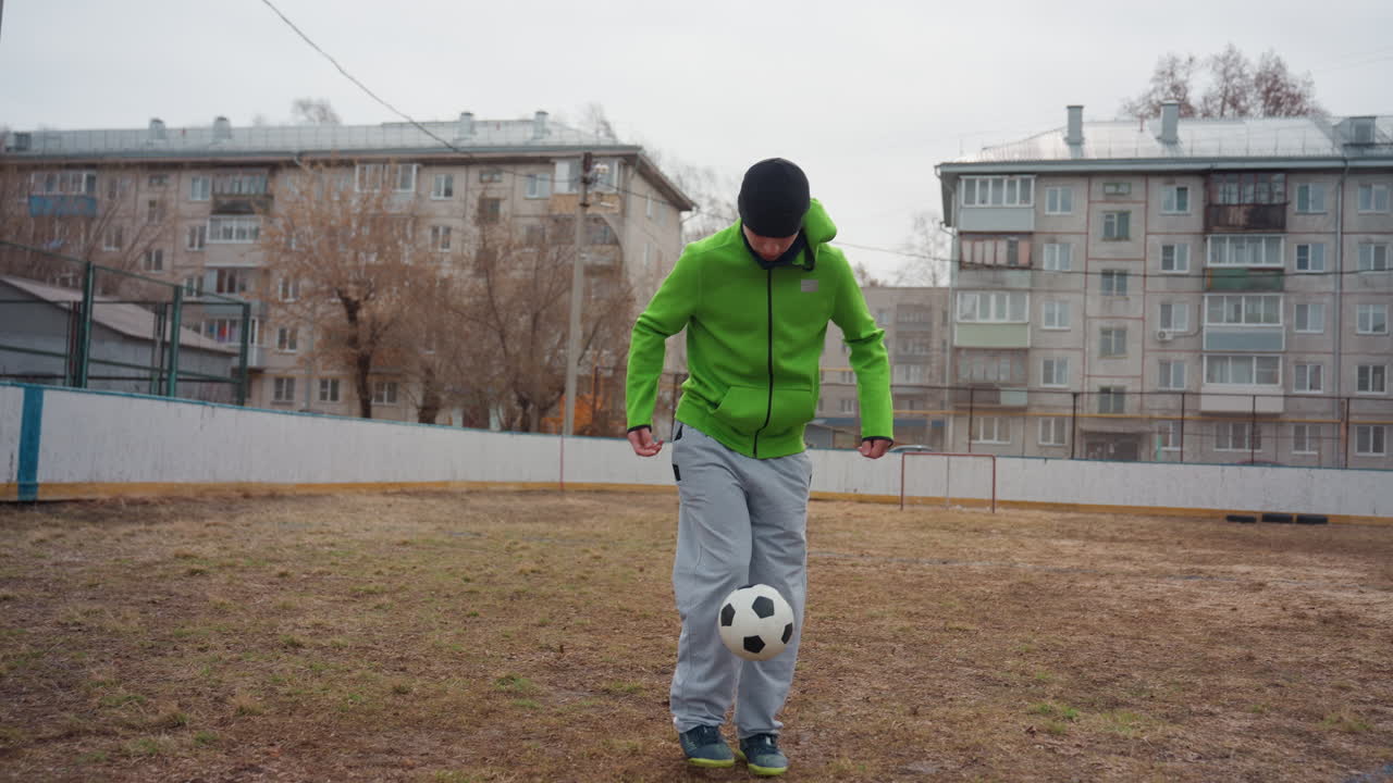 Молодой человек выполняет динамичные удары на открытом воздухе, спортсмен демонстрирует виртуозные трюки на городском спортивном поле, молодой человек в повседневной одежде отрабатывает впечатляющие трюковые удары под пасмурным небом