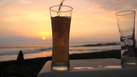 verter cerveza en un vaso en una playa al atardecer