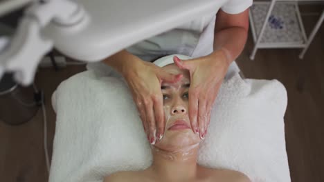 caucasian woman lying back while beautician gives her a facial